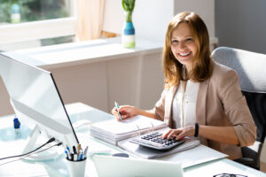 Woman reviewing financial records at a desk with a computer and calculator