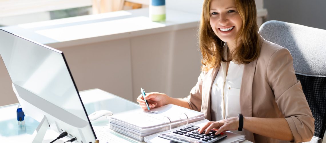 Woman reviewing financial records at a desk with a computer and calculator
