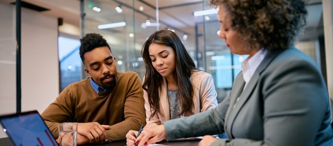 African American woman and her husband signing mortgage agreement during a meeting with their bank manager.